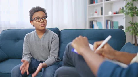 Young boy sitting on couch and speaking to a therapist who is taking notes